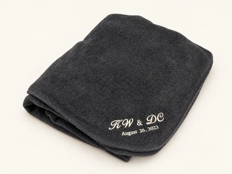 Folded black fleece blanket with initials and a date in the corner